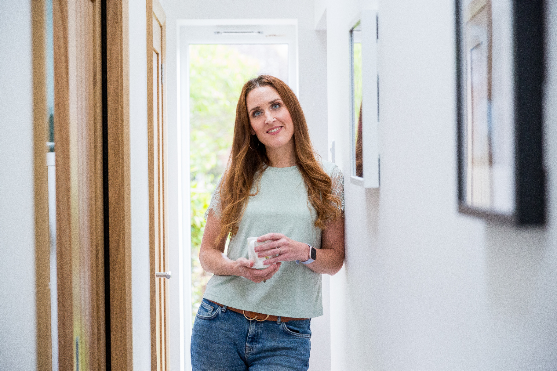 Sam standing in a bright hallway holding a mug